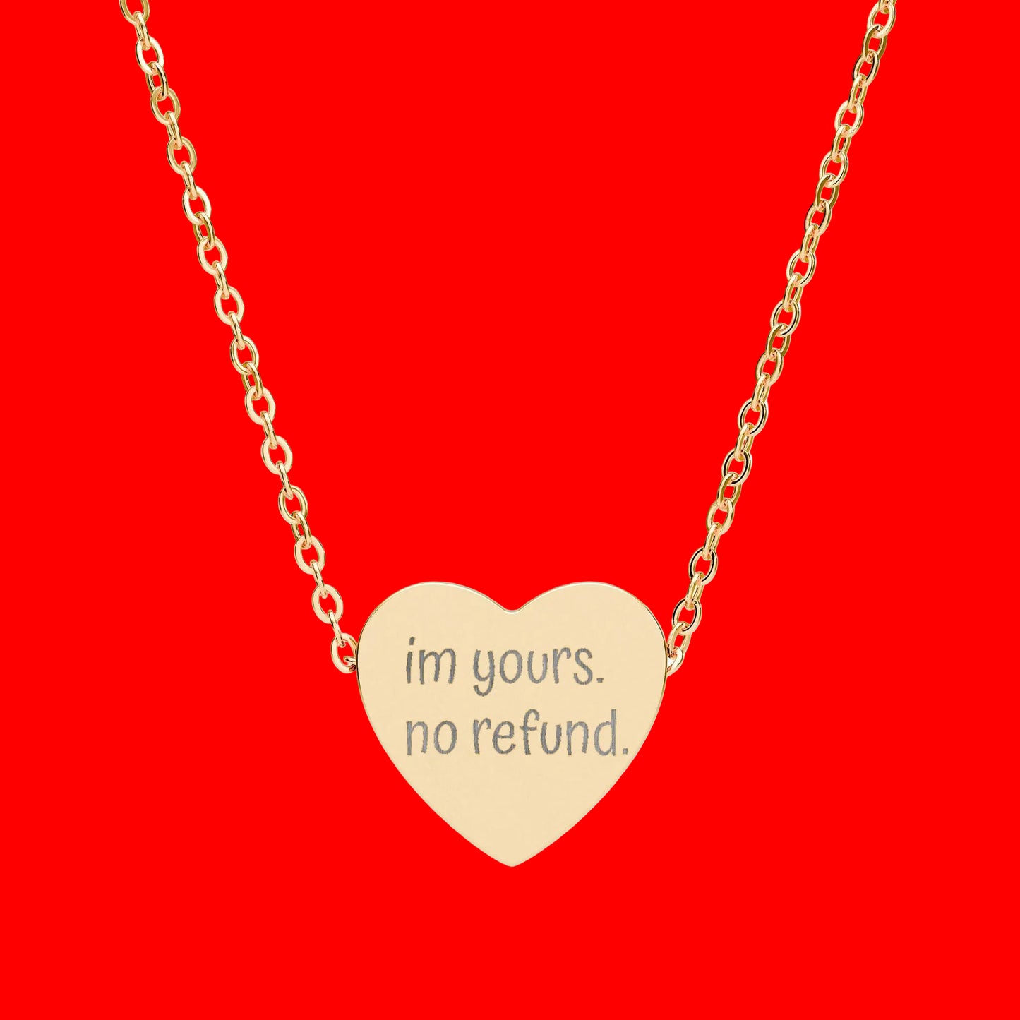 Gold heart-shaped necklace with 'im yours. no refund.' engraving on a white background