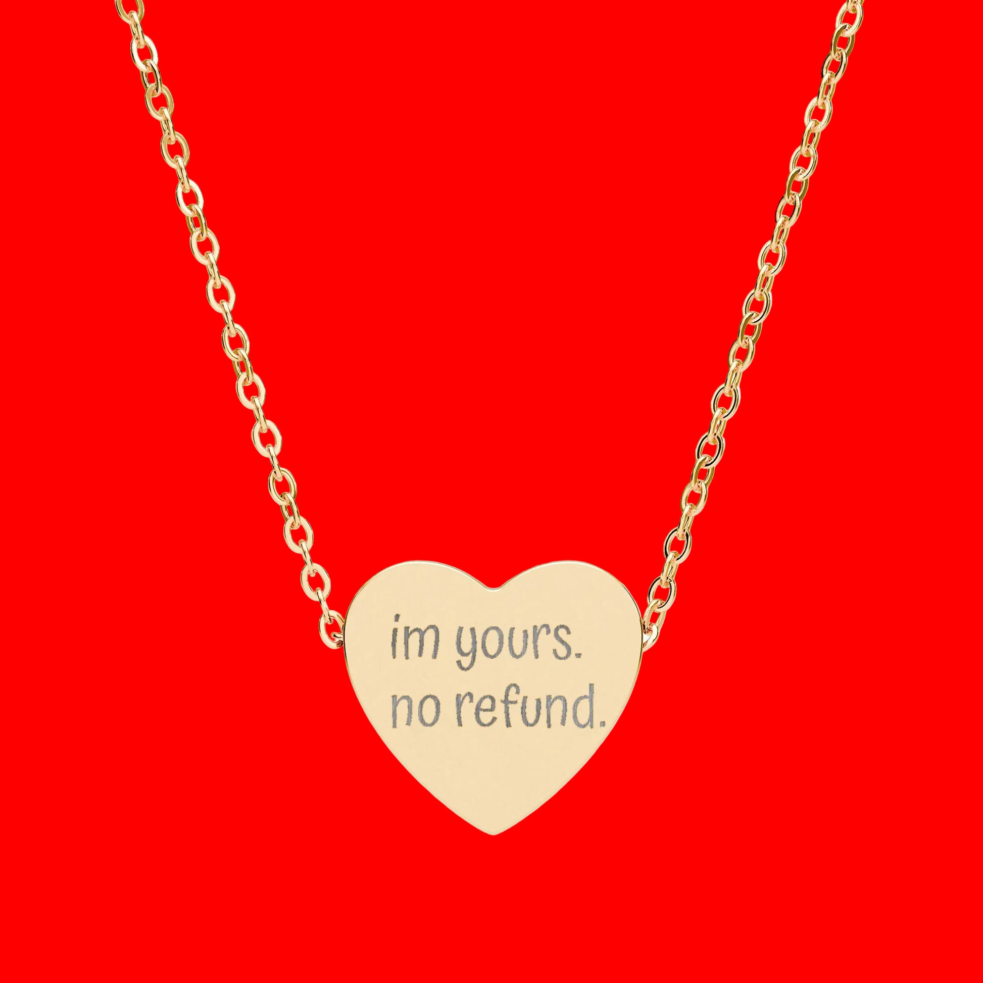 Gold heart-shaped necklace with 'im yours. no refund.' engraving on a white background