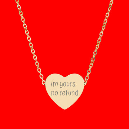 Gold heart-shaped necklace with 'im yours. no refund.' engraving on a white background