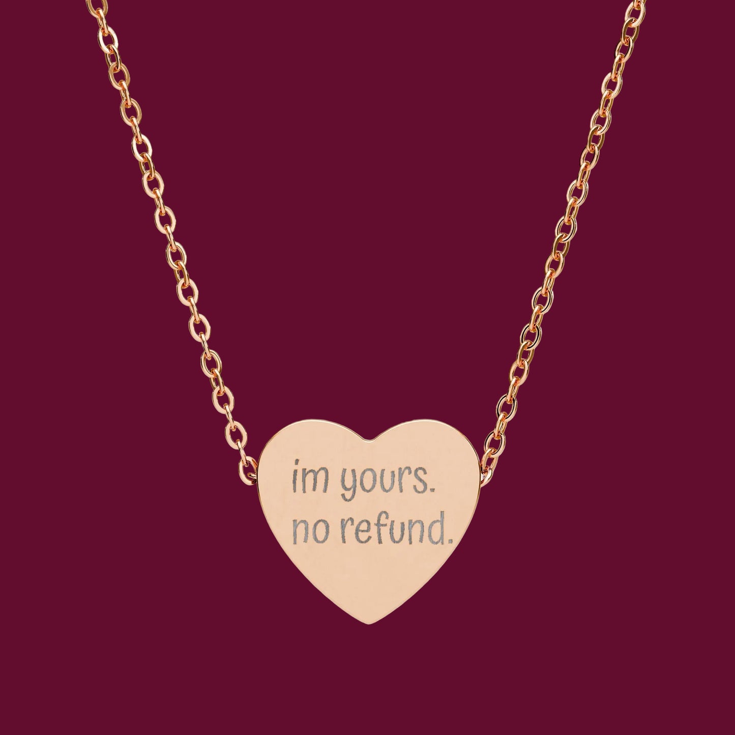 Rose gold heart-shaped necklace with 'im yours. no refund.' engraving on a white background