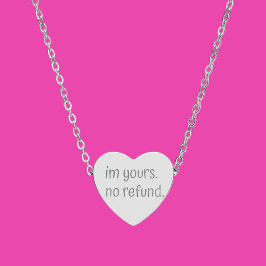 Heart-shaped silver necklace with 'i'm yours. no refund.' engraving on a white background